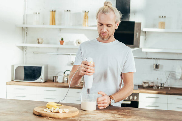 adult man mixing banana protein shake with electric blender at home