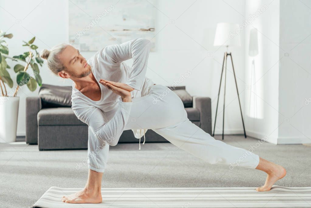 man standing in Revolved Side Angle exercise, Parivrtta Parsvakonasana pose on yoga mat at home