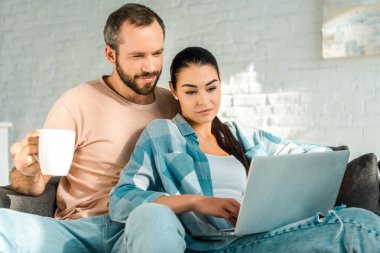 yakışıklı kocam kahve süre kanepede dizüstü kullanarak eş tutan