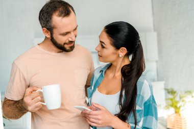 karısı kocası holding evde kahve fincan gülümseyen Smartphone kullanarak