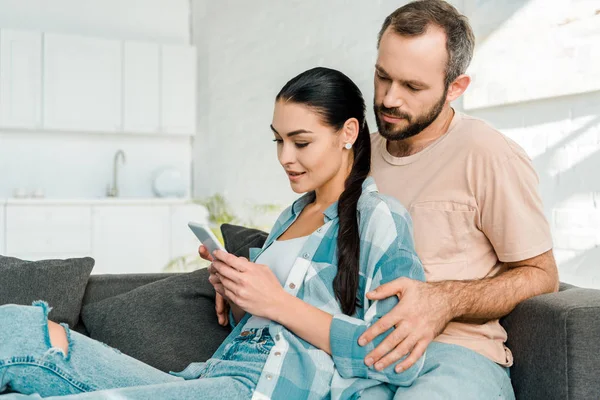 Hermosa Pareja Sentada Sofá Uso Teléfono Inteligente Casa —  Fotos de Stock