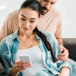 Beautiful couple sitting on couch and using smartphone at home