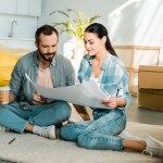 Beautiful couple drinking coffeeand holding blueprint of new house, moving concept