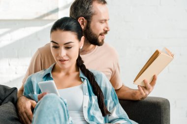 kanepede oturan ve evde kitap okurken erkek ise Smartphone kullanarak çekici karısı
