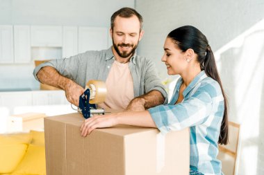 handsome husband and wife packing cardboard box with scotch tape, moving concept