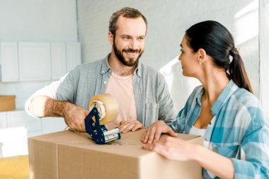 husband and wife packing cardboard box with scotch tape, moving concept clipart