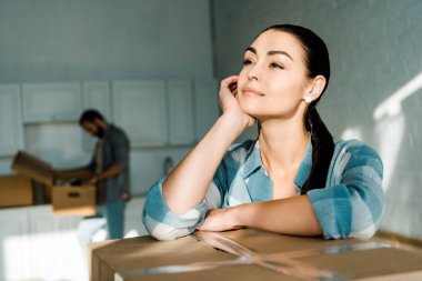 beautiful wife dreaming about new house with husband packing behind, moving concept clipart