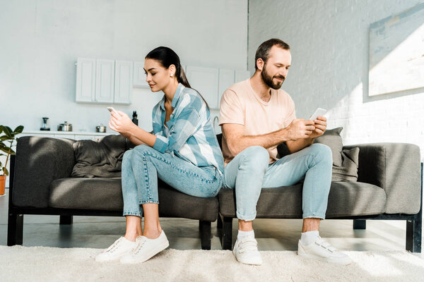 couple sitting on couch, facing opposite direction and using smartphones at home