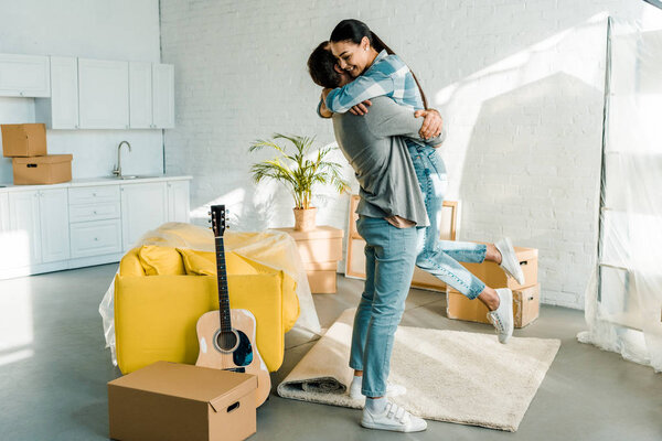 happy husband hugging wife while packing for new house, moving concept