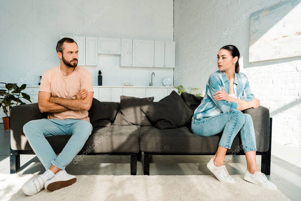 frustrated couple having argument and sitting at opposite ends of sofa