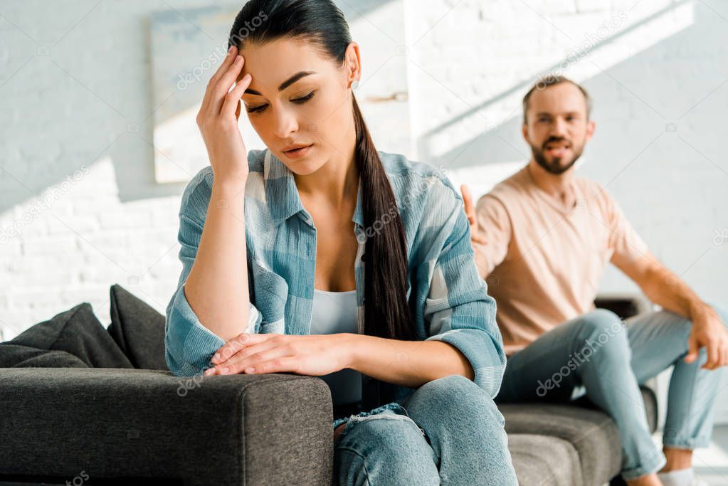 stressed wife with hand on head sitting on foreground after arguing with husband at home