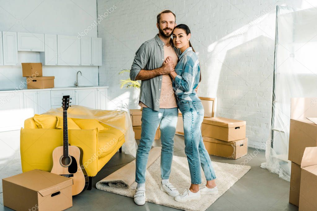 happy couple holding hands and embracing while packing for new house, moving concept