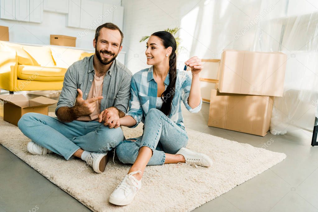 husband pointing finger at wife holding keys from new house, moving concept