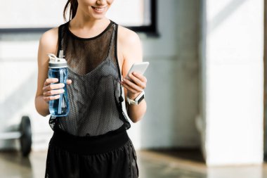 spor şişe su ile tutarak ve spor salonunda smartphone kullanarak uygun sporcumuz kısmi görünümünü