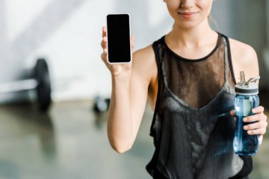 spor şişe tutan ve spor merkezi boş ekran ile smartphone kullanarak gülümseyen sporcumuz kırpılmış görünümünü