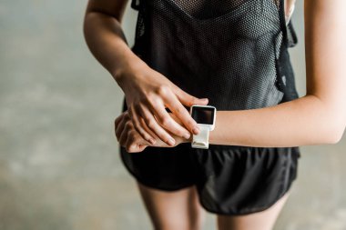 partial view of sportswoman adjusting sport smartwatch with blank screen at gym clipart