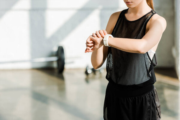midsection of sportswoman adjusting sport smartwatch at gym