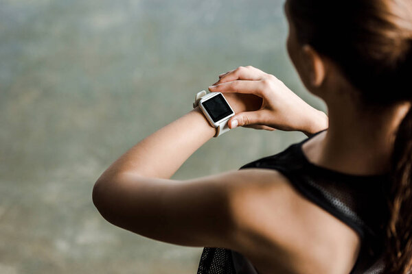 cropped view of sportswoman looking at sport smartwatch with blank screen at gym