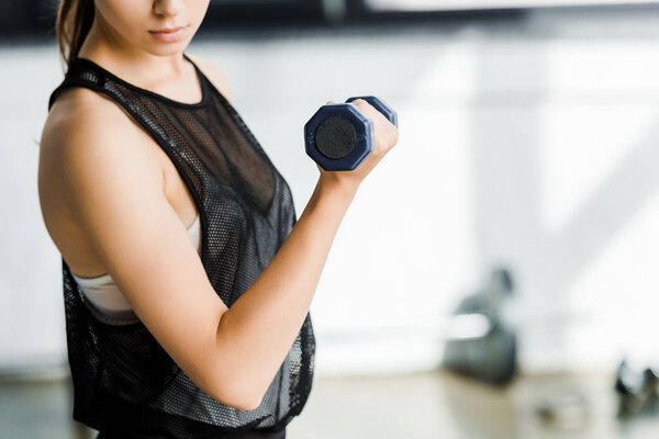 частичный взгляд на тренировку спортсменки с гантелями в фитнес-студии
