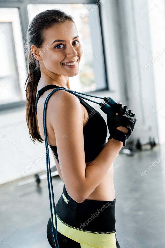portrait of attractive sportswoman looking at camera and holding skipping rope at gym