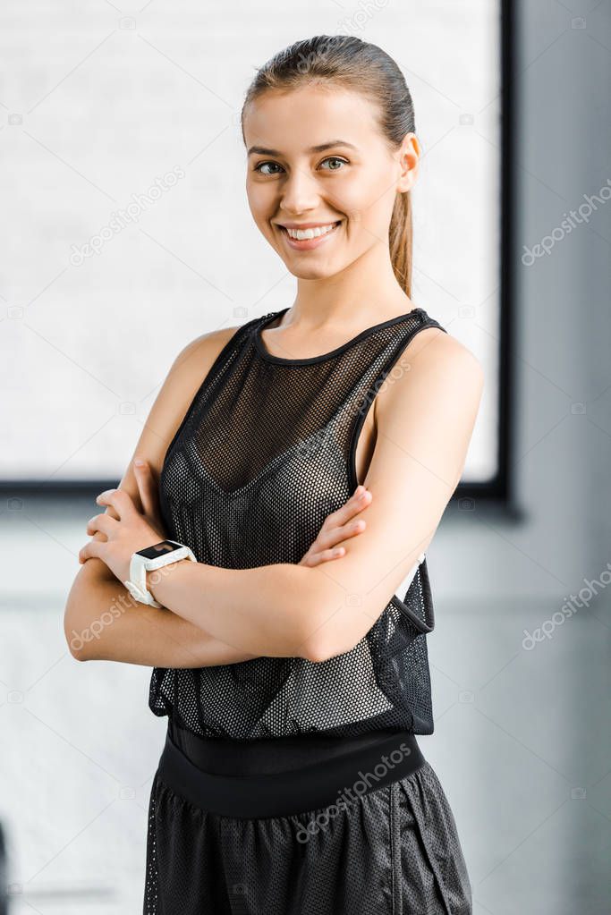 portrait of beautiful sportswoman in black with arms crossed looking at camera at fitness studio