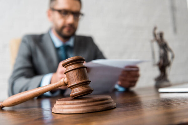 close-up view of wooden hammer and judge working with papers behind 