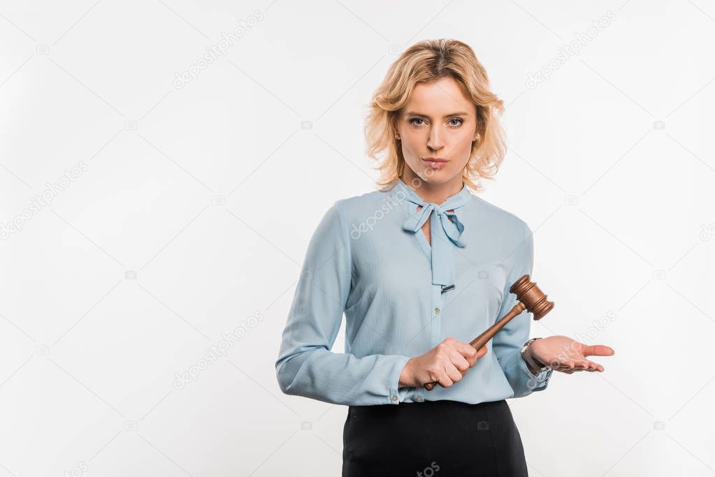 serious female judge holding wooden hammer and looking at camera isolated on white