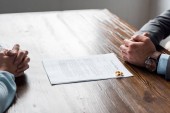 Oříznout záběr rukou advokáta a klienta, rozvod dekret a snubní prsteny na stole 