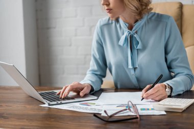 cropped shot of focused businesswoman working with papers and laptop in office    clipart