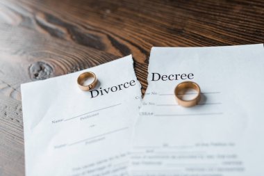 close-up shot of teared divorce decree and engagement rings on wooden surface clipart