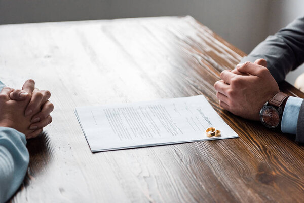 обрезанные руки адвоката и клиента, указ о разводе и обручальные кольца на столе
 