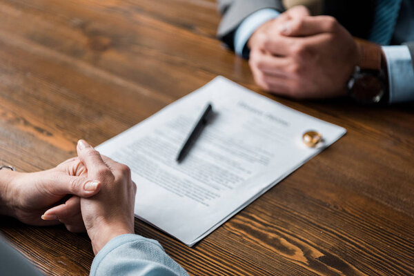 частичный взгляд на адвоката и клиента, сидящего за столом с постановлением о разводе и обручальными кольцами
 