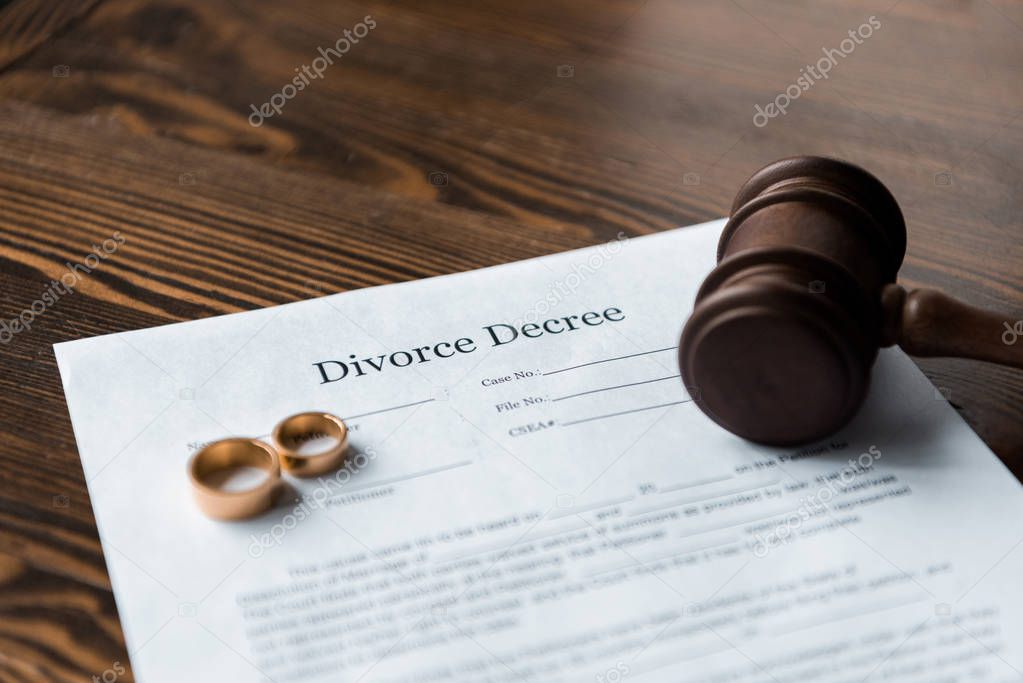 divorce decree, wedding rings and judge hammer on wooden table