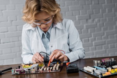 concentrated female computer engineer with tester examining motherboard