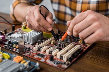 cropped shot of computer engineer with tester examining motherboard clipart