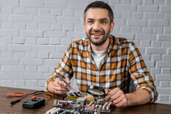 Apuesto Ingeniero Informático Sonriente Con Pinzas Lupa Reparación Placa Base — Foto de stock gratis