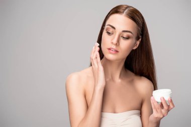 young woman applying face cream on perfect skin, isolated on grey clipart