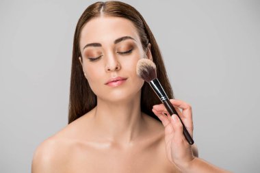 beautiful young woman applying face powder with cosmetic brush, isolated on grey clipart