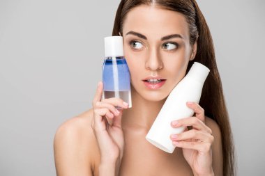 mükemmel cilt makyaj temizleyici, gri izole ile iki şişe tutan güzel kızla