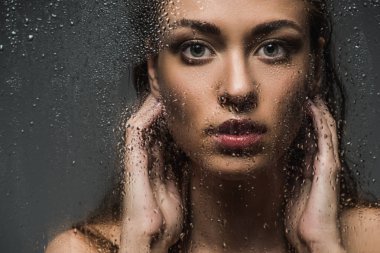 beautiful brunette woman behind wet glass with drops