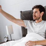Handsome young man taking selfie with smartphone in bed