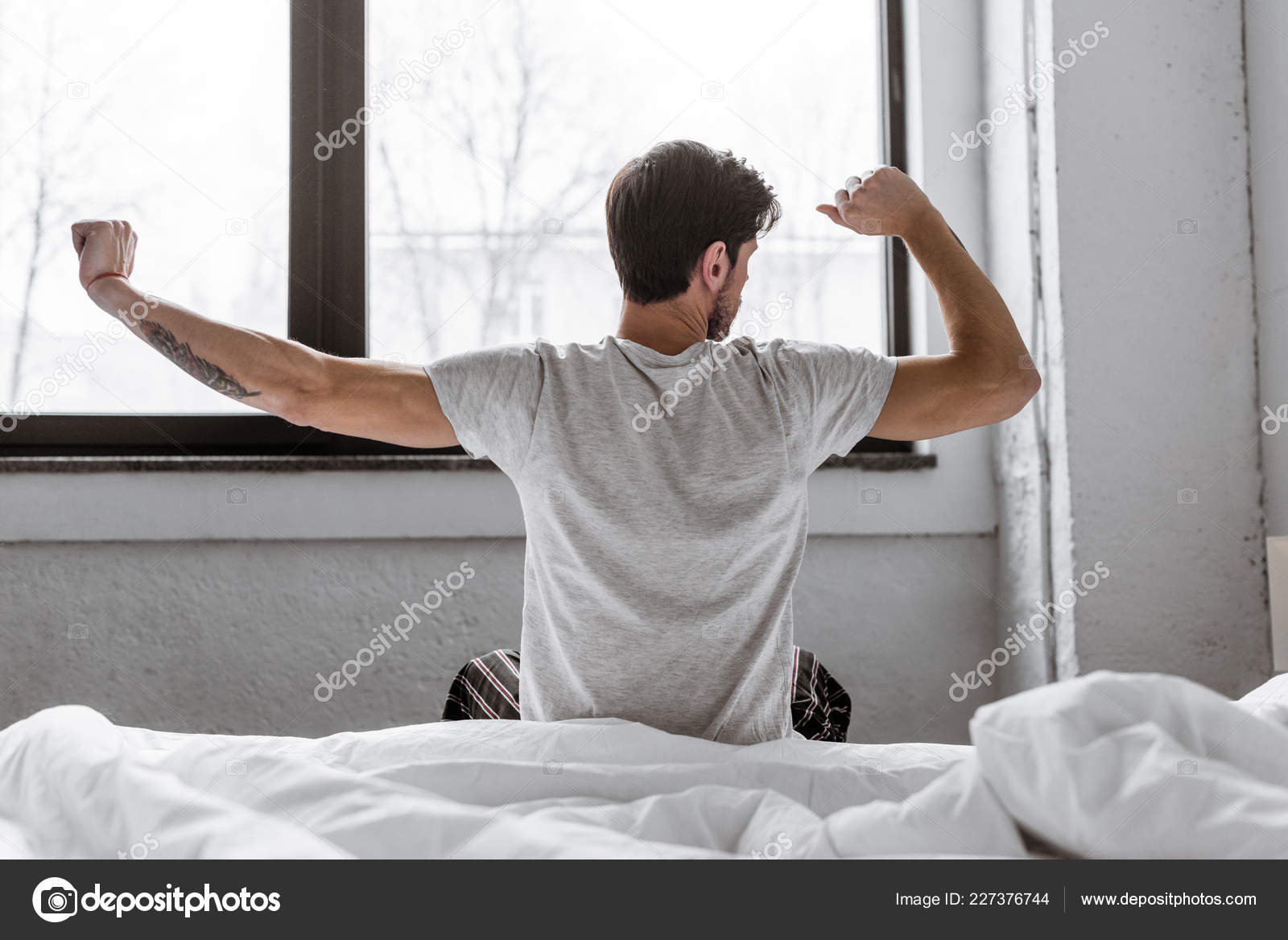 Rear View Young Man Pajamas Stretching While Sitting Bed