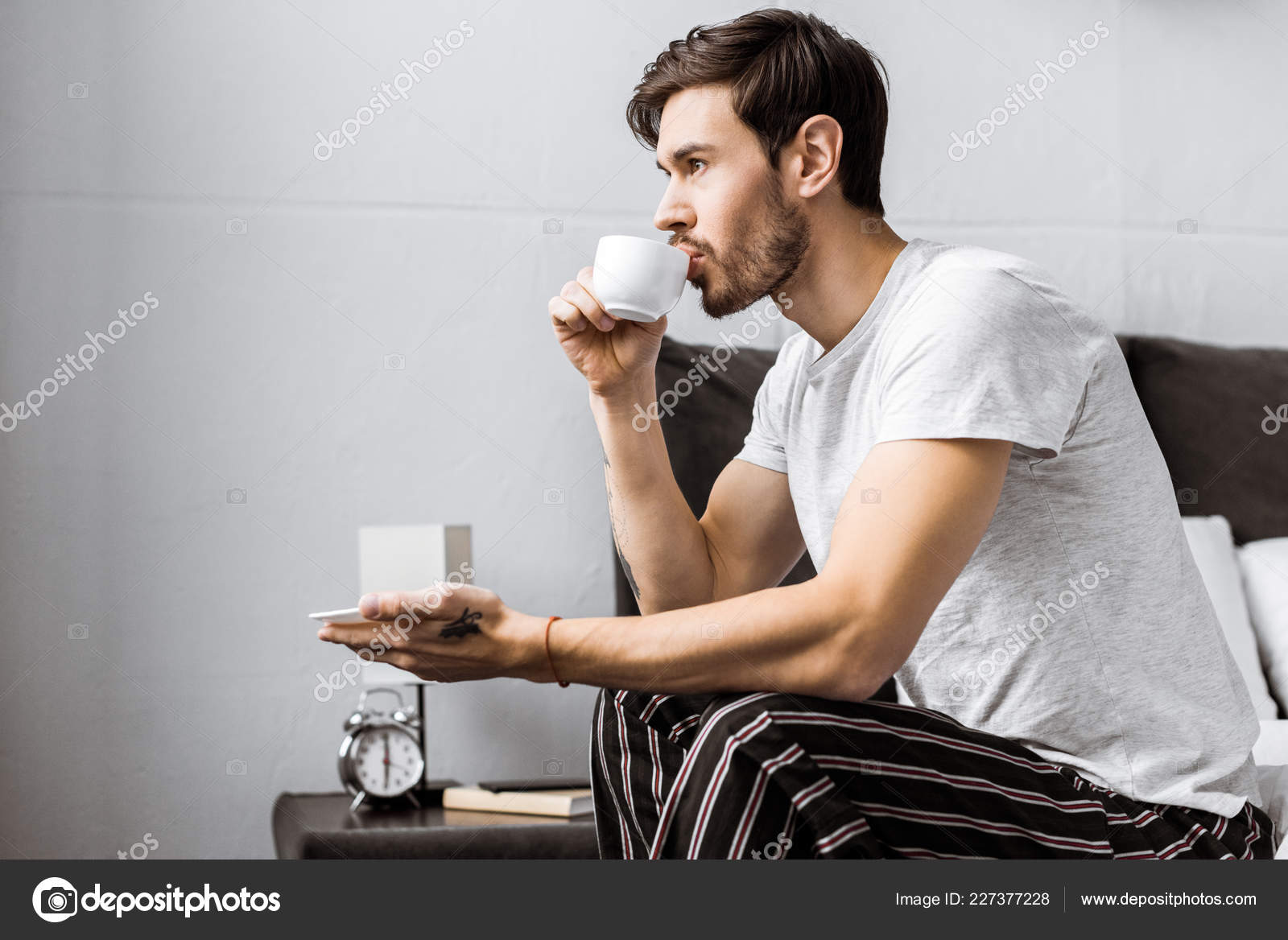 若い男がベッドの上に座って 朝のコーヒーを飲みながらの側面図 無料のストック写真 C Allaserebrina