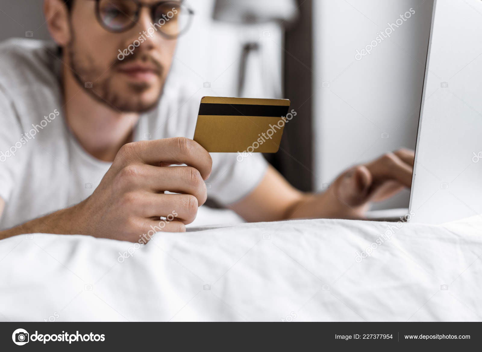 クレジット カードを保持していると ベッドの上のノート パソコンを使用しての眼鏡の若い男のクローズ アップ ビュー 無料のストック写真 C Allaserebrina