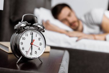 close-up view of alarm clock and young man sleeping behind clipart