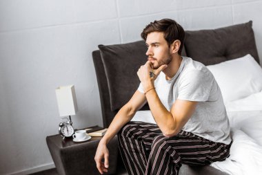 düşünceli genç adam yatakta oturuyor ve uzak sabah seyir pijama