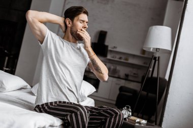 Genç adam esneme ve sabahları yatakta uzanan pijama