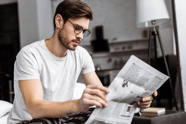 Pijama ve yatağın üstüne oturan ve sabah gazetede Gözlük Genç adam