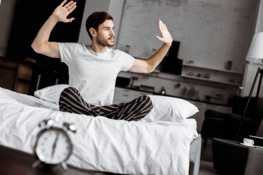 yakışıklı genç adam yatakta oturuyor ve sabah eller yükselterek pijama