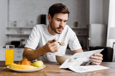 Mısır gevreği kahvaltı için sahip ve evde gazete okurken yakışıklı delikanlı